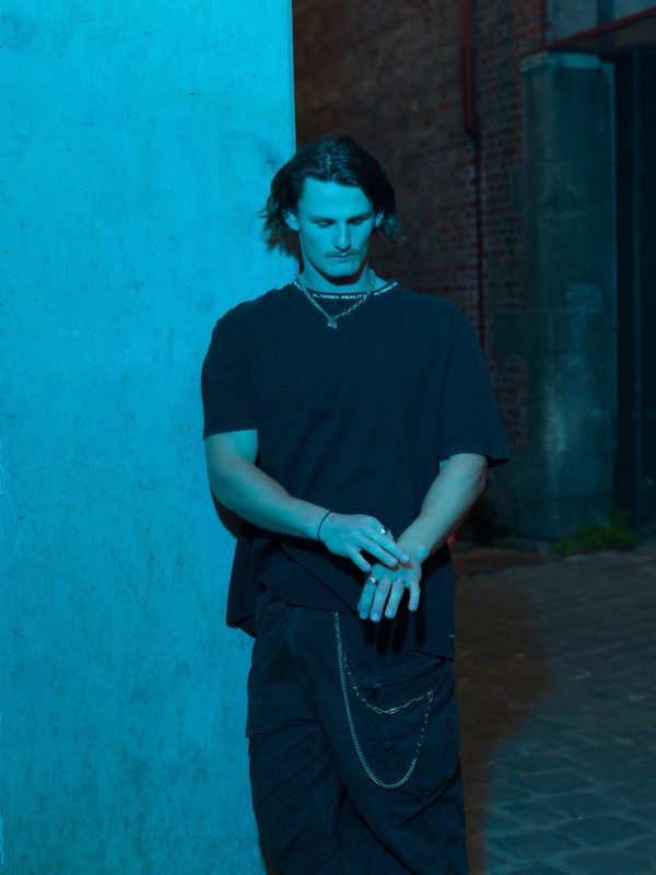 Audent standing against a blue lit wall, press photo